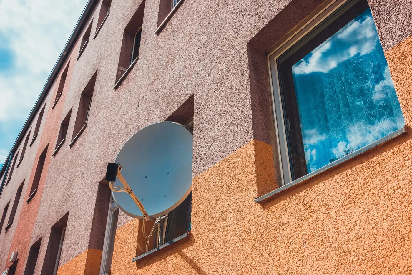 Satellite dish mounted on an apartment building wall beside a window