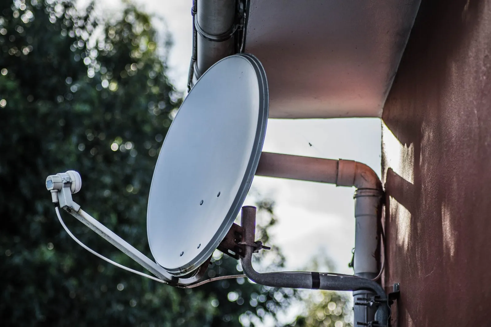 Satellite dish on a wall bracket under a roof eave
