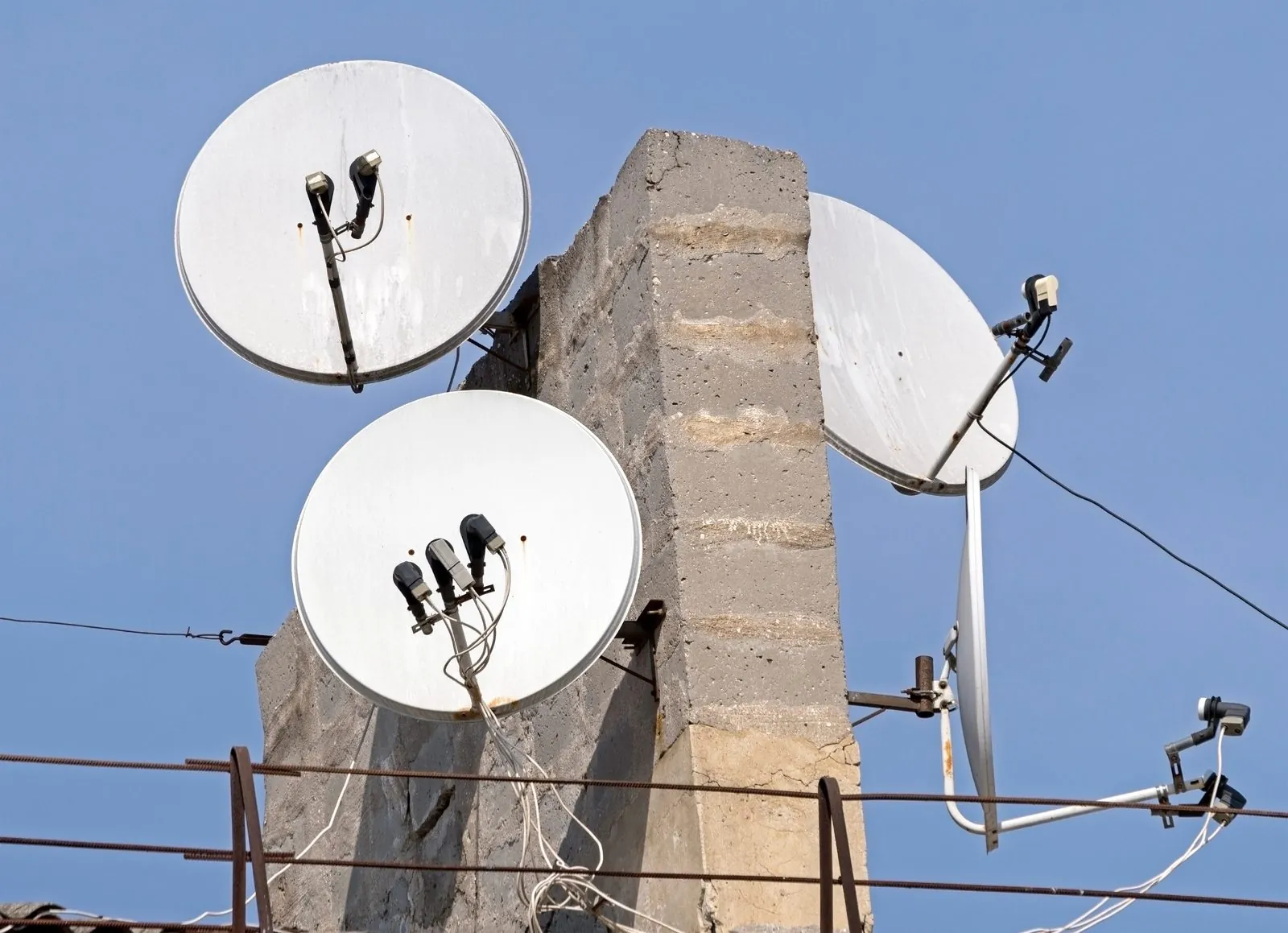 Several satellite dishes mounted on a rooftop mast and wall