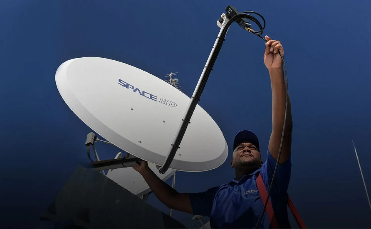Technician reaching up to fit a satellite dish on a mast against a blue sky