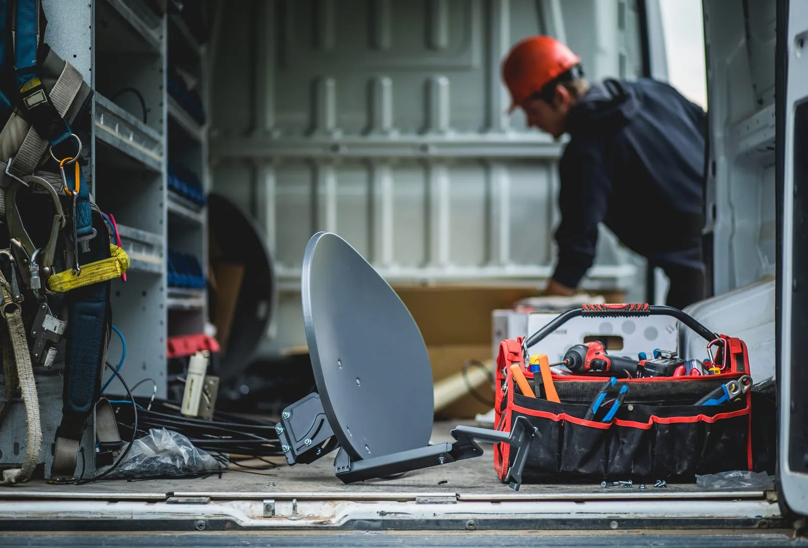 Technician working in the back of a service van with a satellite dish and tool bag